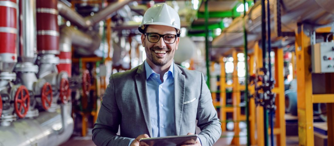 handsome-smiling-supervisor-gray-suit-with-white-helmet-head-holding-tablet-power-plant-interior