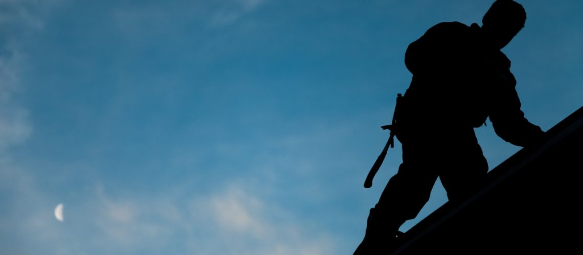 Contractor,In,Silhouette,Working,On,A,Roof,Top,With,Blue